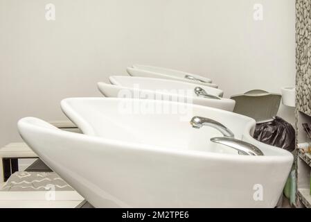 Rangée d'éviers en porcelaine blanche pour laver les cheveux dans un salon de coiffure avec robinets et tuyaux Banque D'Images