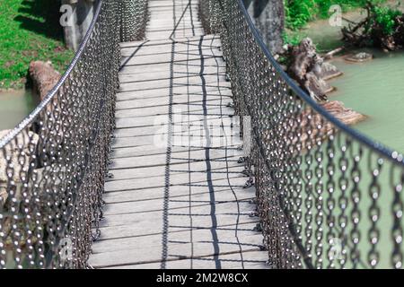 Footbridge over the river . Pedestrian bridge made by chains and wooden planks . Hanging walkway Stock Photo