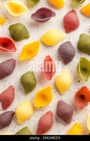 Fond de pâtes colorées. Vue du dessus des coquilles de pâtes cinq couleurs sur fond de pierre blanche. Pâtes au curcuma, aux épinards, à la betterave et à la carotte noire Banque D'Images