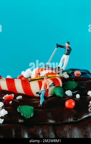 gros plan d'un homme miniature qui skine et d'une femme miniature qui porte ses skis sur son épaule, sur un gâteau de bûche de yule sur fond bleu Banque D'Images