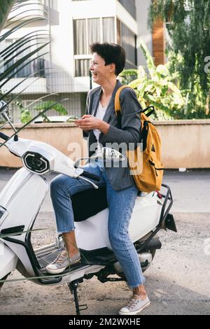 Une femme d'âge moyen prend son scooter blanc. Banque D'Images