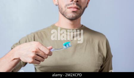 Un gars au visage méconnaissable tient une brosse à dents avec du dentifrice sur un fond isolé, montre brosse à dents Banque D'Images