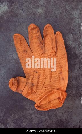 Gants en caoutchouc ou en latex orange sales et écrasés posés sur du métal terni Banque D'Images