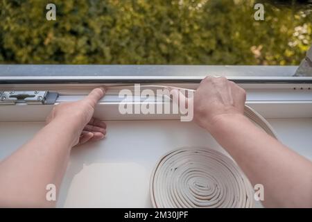 Installation d'une isolation imperméable. un employé colle du ruban de mousse d'étanchéité sur la fenêtre intérieure Banque D'Images