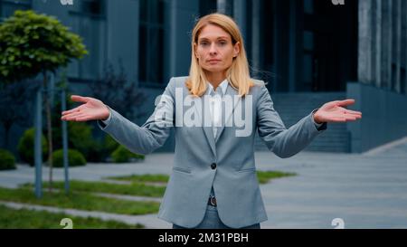 Confuse sérieuse pensive perplexe femme d'affaires debout à l'extérieur des bras des haussières incertain femme caucasienne ne sait pas réponse regarde la caméra Banque D'Images