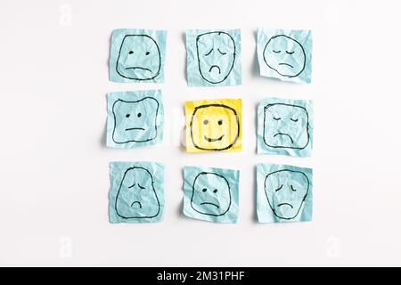 Un triste visage regardant des visages souriants de loin. Visages heureux et tristes dessinés sur des autocollants bleus. Concepts d'exclusion, de différence, de jalousie. Pho de haute qualité Banque D'Images
