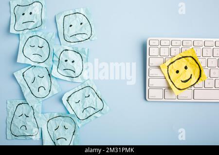 Un triste visage regardant des visages souriants de loin. Visages heureux et tristes dessinés sur des autocollants bleus. Concepts d'exclusion, de différence, de jalousie. Pho de haute qualité Banque D'Images