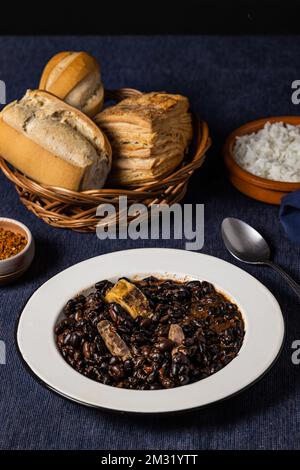 Haricots et porc, cuisine brésilienne typique, sur nappe bleu foncé. Banque D'Images