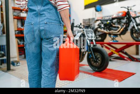 Vue arrière de la mécanicien tenant jerry CAN devant les motos à l'usine Banque D'Images