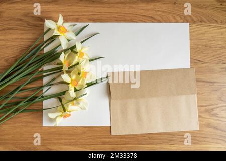 Jonquilles fleurs à plat et mise en page de lettre vierge avec enveloppe sur fond blanc de papier pastel. Concept minimaliste créatif, vue de dessus, espace de copie Banque D'Images