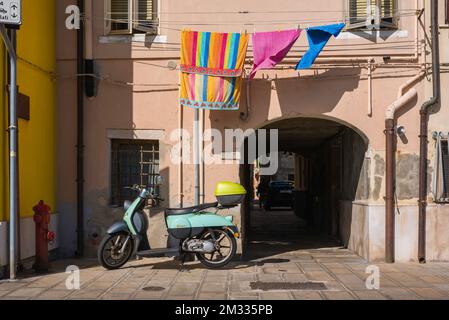 Rue Italie, vue en été d'un scooter stationné contre un mur rose avec une buanderie colorée suspendue au-dessus, Chioggia, Comune de Venise, Vénétie, Italie Banque D'Images