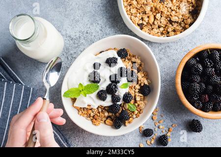 Bol de granola avec yaourt grec et mûres. Main d'homme tenant une cuillère sur un bol à céréales pour le petit déjeuner. Vue de dessus Banque D'Images