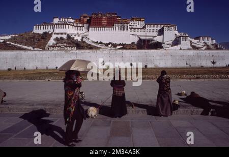 Femmes vêtues de robes traditionnelles avec leur chien et un parapluie devant le Grand Palais du Potala à Lhassa, Tibet, Chine. Banque D'Images
