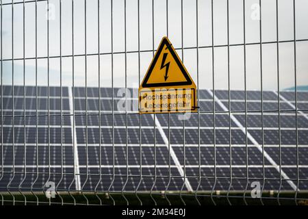 Une clôture sur le fond des panneaux solaires avec un signe allemand: Haute tension, danger de vie Banque D'Images