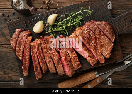 Steaks. Steak de viande grillé en tranches New York ou Ribeye aux épices romarin et poivre sur un plateau en marbre noir sur fond de bois ancien. Vue de dessus. Maquette Banque D'Images