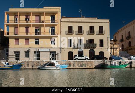 Au port de Mazara del Vallo il y a deux maisons au bord de la rivière contre un ciel bleu. Les maisons ont de nombreuses fenêtres et balcons. Les anciens bateaux sont fixés Banque D'Images