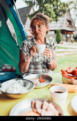 Famille prenant le petit déjeuner à l'extérieur sur le camping pendant les vacances d'été. Pain, fromage cottage, viande froide, tomates, fruits et tasses de café sur table. Fermer Banque D'Images