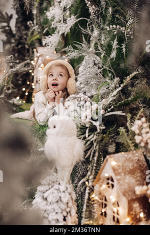 photo de la petite fille se demande dans des vêtements légers se trouve sur une décoration de noël avec des arbres et un petit hibou blanc Banque D'Images