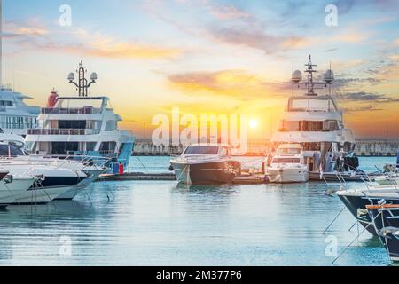 Parking maritime de bateaux à moteur modernes et d'eau bleue. Yachts de luxe amarrés dans le port de mer au coucher du soleil. Tranquillité, détente et vacances à la mode Banque D'Images