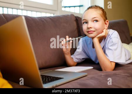 Blonge cheveux petite fille en utilisant un ordinateur portable, faisant des devoirs à la maison.Retour à l'école concept Banque D'Images