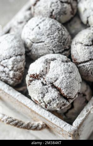 Petits gâteaux craquelés aux pépites de chocolat en gros plan. Boîte rustique en bois avec biscuits secs au chocolat frais dans du sucre glace. Orientation verticale Banque D'Images