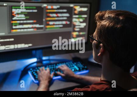 Vue arrière du codage MAN pour la cyber-sécurité, la programmation et le travail à domicile tard dans la nuit. Programmeur, code et employé indépendant des heures supplémentaires travaillant à l'écran du pc en utilisant le langage php. Mise au point sélective Banque D'Images