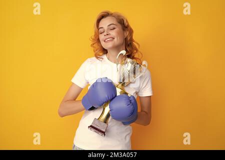 Boxeur féminin primé isolé sur fond jaune. Gagnant succès femme de pouvoir concept. Une femme heureuse en gants de boxe tient le trophée de la coupe gagnante du champion. Banque D'Images