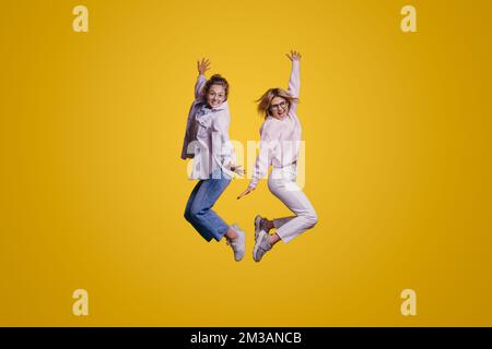 Portrait de taille de corps complet de deux femmes positives adorables et belles qui sautent isolées sur fond jaune levant les mains vers le haut. Belle fille attrayante Banque D'Images