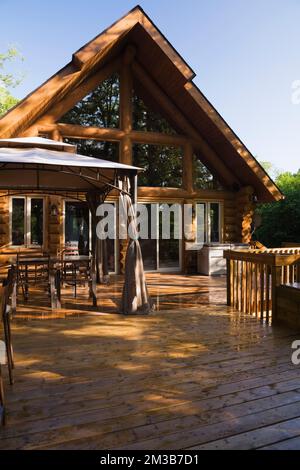 Chalet en rondins de style cadre en a avec terrasse en bois arrosée en été. Banque D'Images