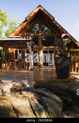 Chalet en rondins de style cadre en a avec terrasse en bois arrosée en été. Banque D'Images