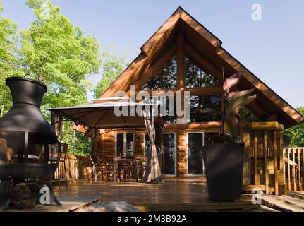 Chalet en rondins de style cadre en a avec terrasse en bois arrosée en été. Banque D'Images