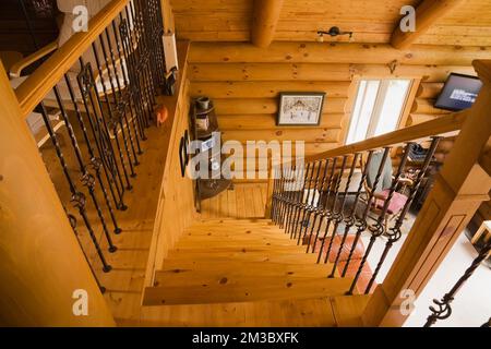 Escalier en bois et balustrade avec balustres en fer forgé menant de la chambre principale à l'étage au salon du rez-de-chaussée à l'intérieur de la cabane en rondins. Banque D'Images