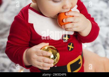 bébé du nouvel an en costume de père noël avec mandarines Banque D'Images