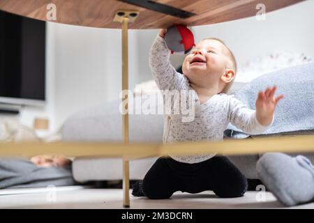 Mignon bébé garçon jouant avec le ballon suspendu, rampant et debout près de la table du salon à la maison. Centre d'activités et de jeux pour les jeunes enfants. Bébé jouant à la maison Banque D'Images