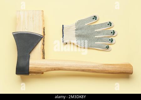 Hache avec bois de chauffage et gants sur fond jaune Banque D'Images