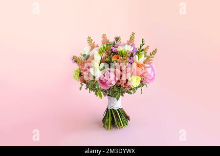 Bouquet de mariage avec pivoines, astilbe, freesia, roses de pivoines Juliette, limonium, dianthus et Pittosporum verts sur fond rose. Vue avant Banque D'Images