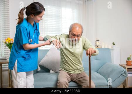 Infirmière soignante aidant à soutenir un homme handicapé senior à se lever avec un bâton de marche Banque D'Images