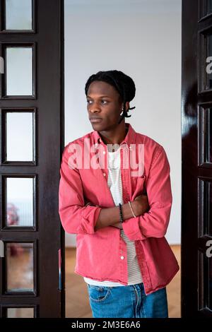 Jeune homme africain pensif debout avec des armes croisées à la maison pensant à la décision difficile Banque D'Images