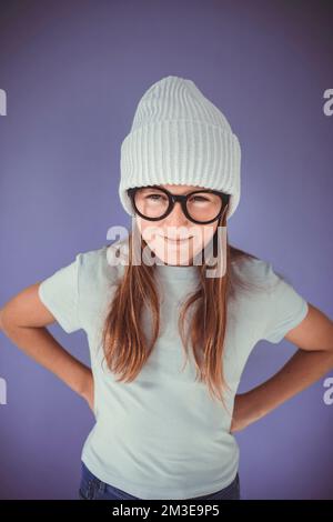 jeune fille avec des lunettes épaisses et un bonnet devant un fond violet Banque D'Images