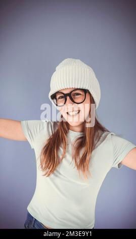 jeune fille avec des lunettes épaisses et un bonnet devant un fond violet Banque D'Images