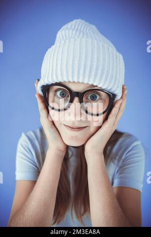 jeune fille avec des lunettes épaisses et un bonnet devant un fond violet Banque D'Images