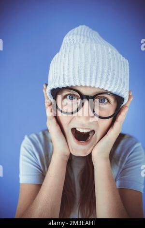 jeune fille avec des lunettes épaisses et un bonnet devant un fond violet Banque D'Images