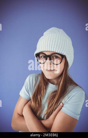 jeune fille avec des lunettes épaisses et un bonnet devant un fond violet Banque D'Images