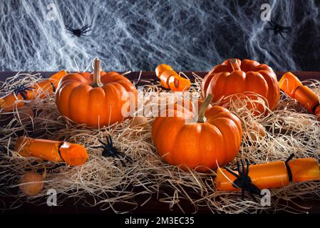 Citrouilles, bonbons, araignées et toile d'araignée décorée de paille sur fond noir, concept de fête d'Halloween Banque D'Images