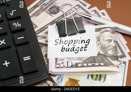 Concept financier et commercial. Sur fond marron se trouve une calculatrice et des dollars sur un clip avec une inscription sur papier - Budget de shopping Banque D'Images