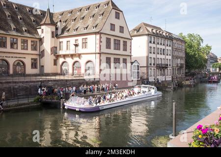 Touristes dans un bateau touristique à l'ancienne maison de douane sur la rivière Ill par une journée ensoleillée à Strasbourg, France. C'est maintenant un marché agricole appelé la Nouvelle Douane. Banque D'Images