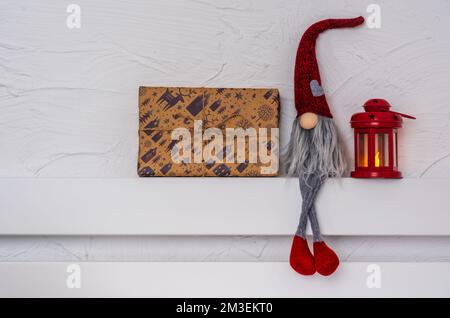 Christmas Gnom - Gonk avec une longue barbe et un chapeau rouge assis sur la tablette en bois blanc avec pattes de suspension. Concept Noël et nouvel an, carte de vœux, Banque D'Images
