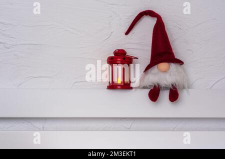 Christmas Gnom - Gonk avec une longue barbe et un chapeau rouge assis sur la tablette en bois blanc avec pattes de suspension. Concept Noël et nouvel an, carte de vœux, Banque D'Images