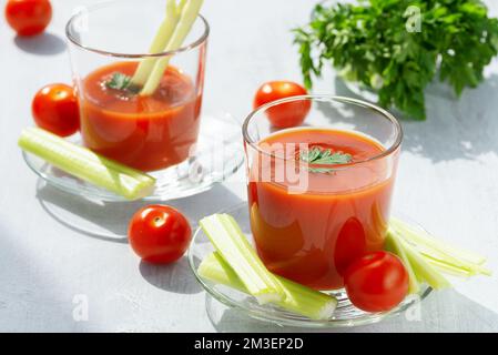 Deux verres avec jus de tomate frais, céleri, persil et tomates mûres Banque D'Images