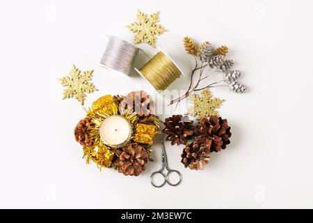 Set pour faire des décorations de Noël sur la table de ciseaux, bijoux, ruban, cônes et bougies sur un fond beige Banque D'Images